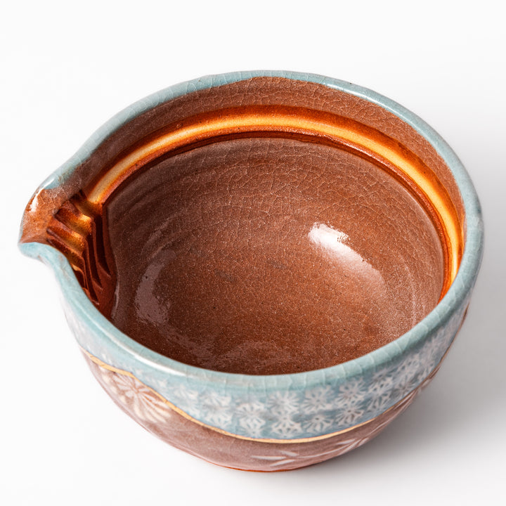 Ceramic teapot with lid featuring a turquoise crackle glaze and floral patterns in soft brown tones accented by a curved gold line.