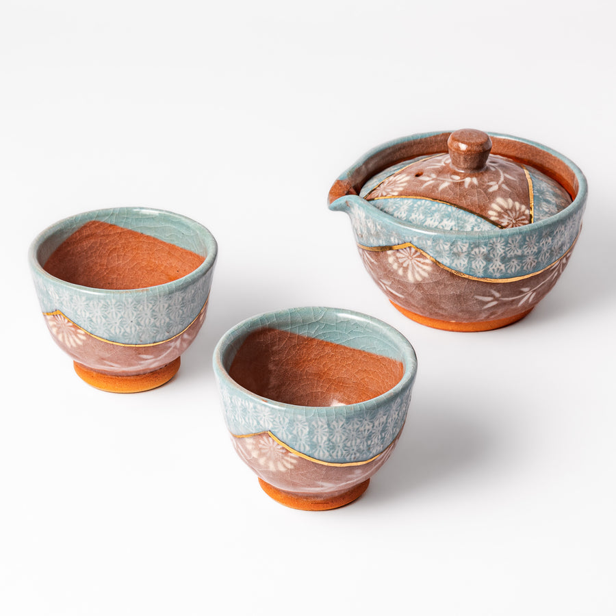 Three piece ceramic tea set with floral patterns and a turquoise crackle glaze, featuring a spouted teapot and two matching cups.