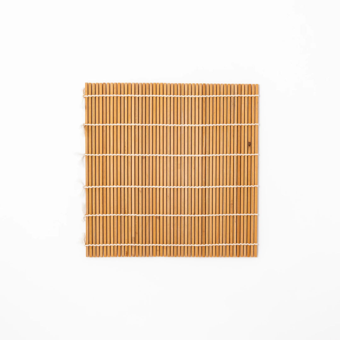 Traditional bamboo sushi rolling mat with uniform slats and white cotton string, partially rolled to show flexibility for making perfect sushi at home.