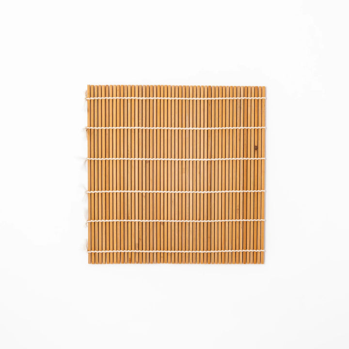 Traditional bamboo sushi rolling mat with uniform slats and white cotton string, partially rolled to show flexibility for making perfect sushi at home.