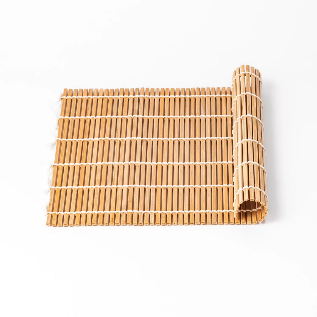 Traditional bamboo sushi rolling mat with uniform slats and white cotton string, partially rolled to show flexibility for making perfect sushi at home.