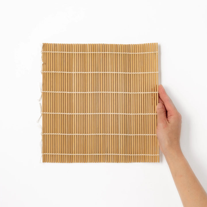 Bamboo sushi rolling mat with smooth, evenly spaced slats and white cotton string, perfect for shaping homemade sushi rolls with traditional style.
