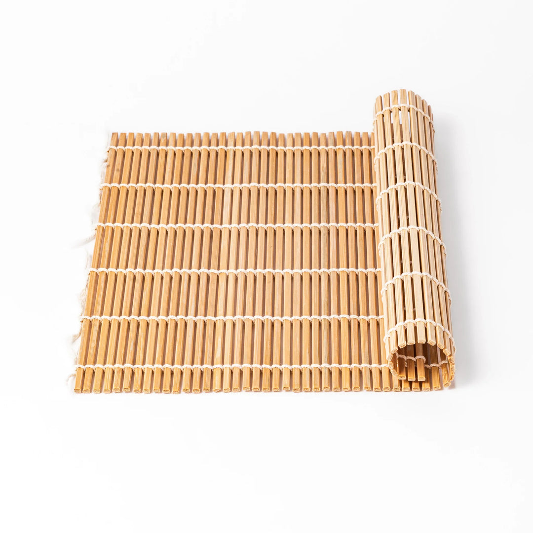 Bamboo sushi rolling mat with smooth, evenly spaced slats and white cotton string, perfect for shaping homemade sushi rolls with traditional style.


