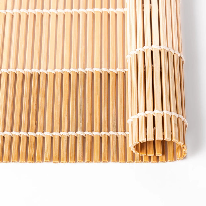 Bamboo sushi rolling mat with smooth, evenly spaced slats and white cotton string, perfect for shaping homemade sushi rolls with traditional style.

