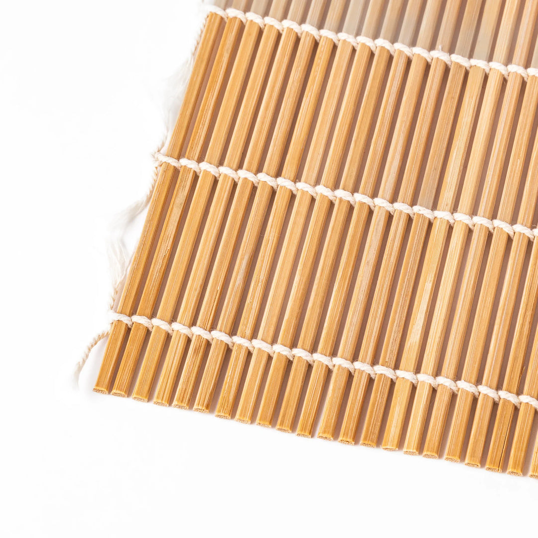 Bamboo sushi rolling mat with smooth, evenly spaced slats and white cotton string, perfect for shaping homemade sushi rolls with traditional style.

