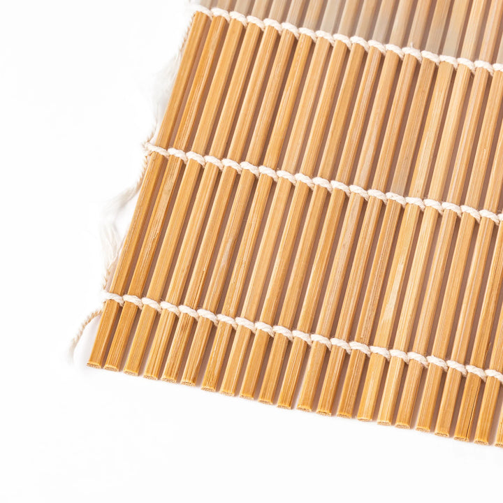 Bamboo sushi rolling mat with smooth, evenly spaced slats and white cotton string, perfect for shaping homemade sushi rolls with traditional style.
