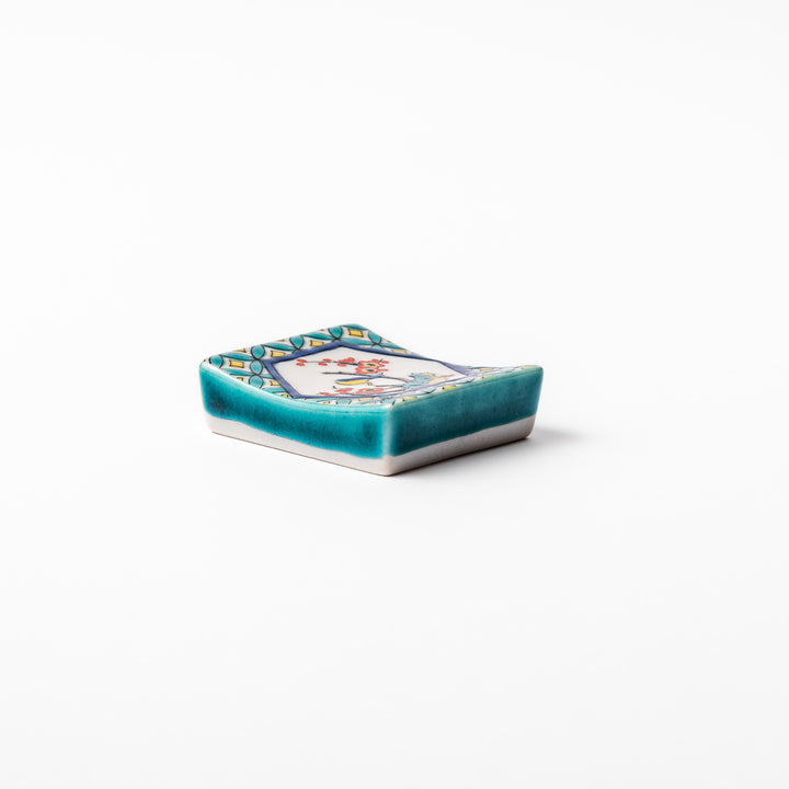 Rectangular Japanese ceramic chopstick rest with turquoise border and central motif of bird on plum blossoms in vivid colors.