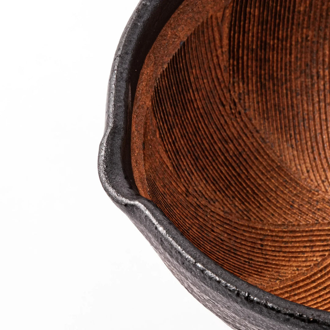 Black ceramic suribachi mortar bowl with rough-textured brown interior grooves and spout, ideal for grinding sesame seeds and other seasonings with precision.