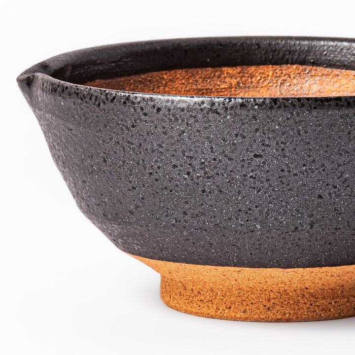 Black ceramic suribachi mortar bowl with rough-textured brown interior grooves and spout, ideal for grinding sesame seeds and other seasonings with precision.