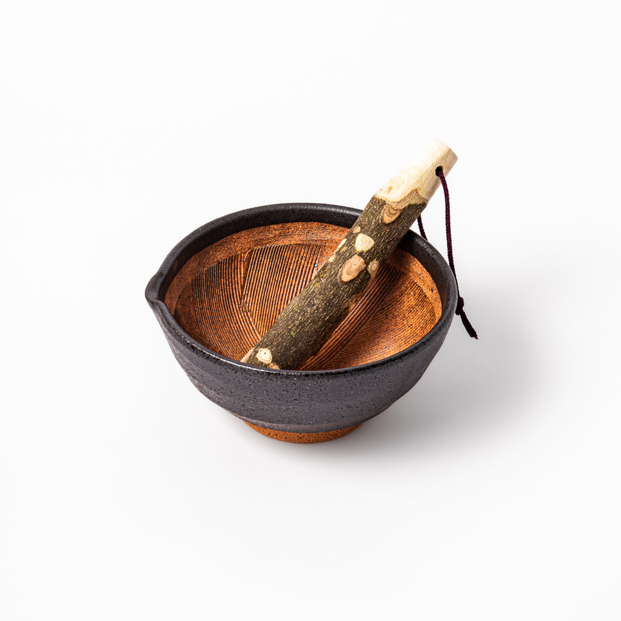 Black ceramic suribachi mortar with grooved brown interior and natural wood pestle, perfect for grinding sesame seeds and spices in traditional style.