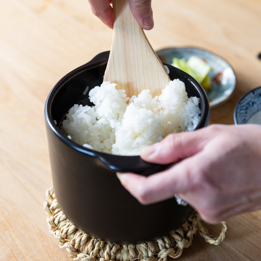 Fluffing freshly cooked Japanese rice in black microwave rice cooker with double lid