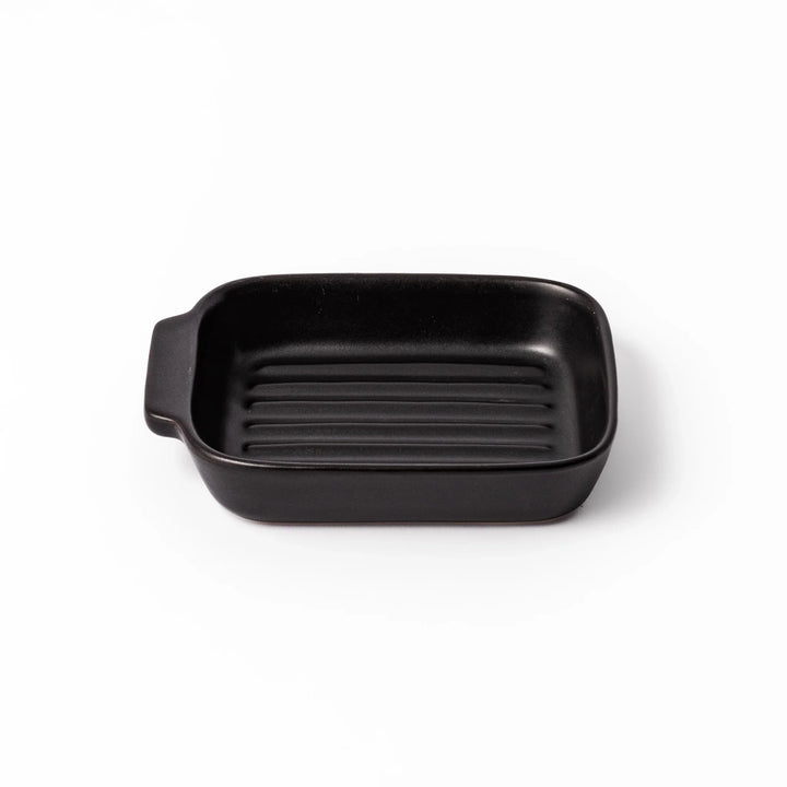Rectangular black ceramic baking dish with ridged base and side handle, designed for oven use and versatile table presentation.