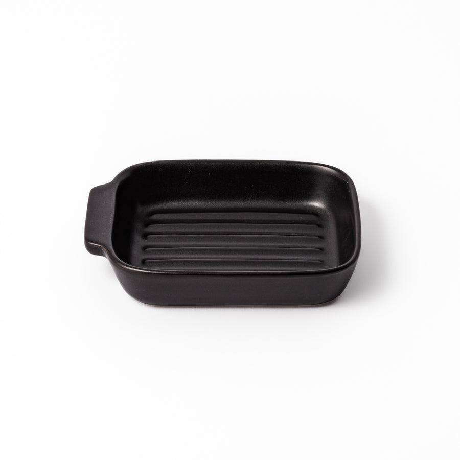 Rectangular black ceramic baking dish with ridged base and side handle, designed for oven use and versatile table presentation.