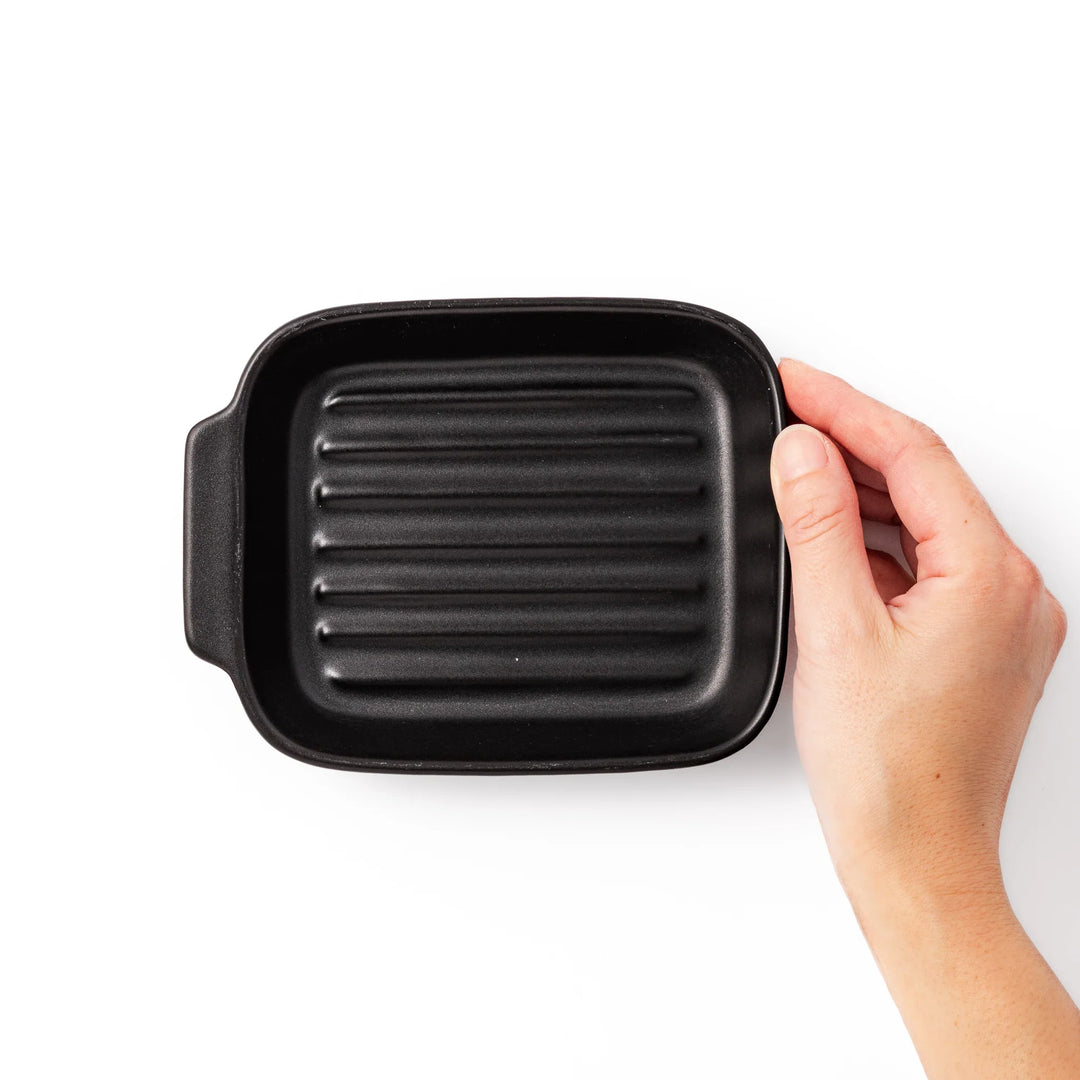 Rectangular black ceramic baking dish with ridged base and side handle, designed for oven use and versatile table presentation.