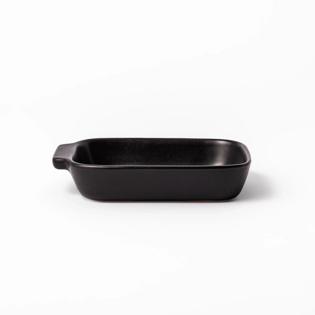 Rectangular black ceramic baking dish with ridged base and side handle, designed for oven use and versatile table presentation.