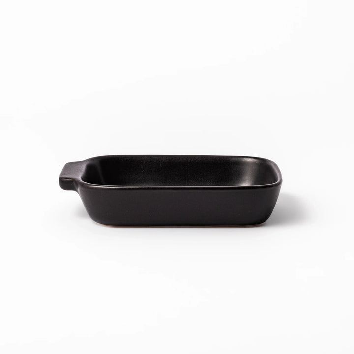 Rectangular black ceramic baking dish with ridged base and side handle, designed for oven use and versatile table presentation.