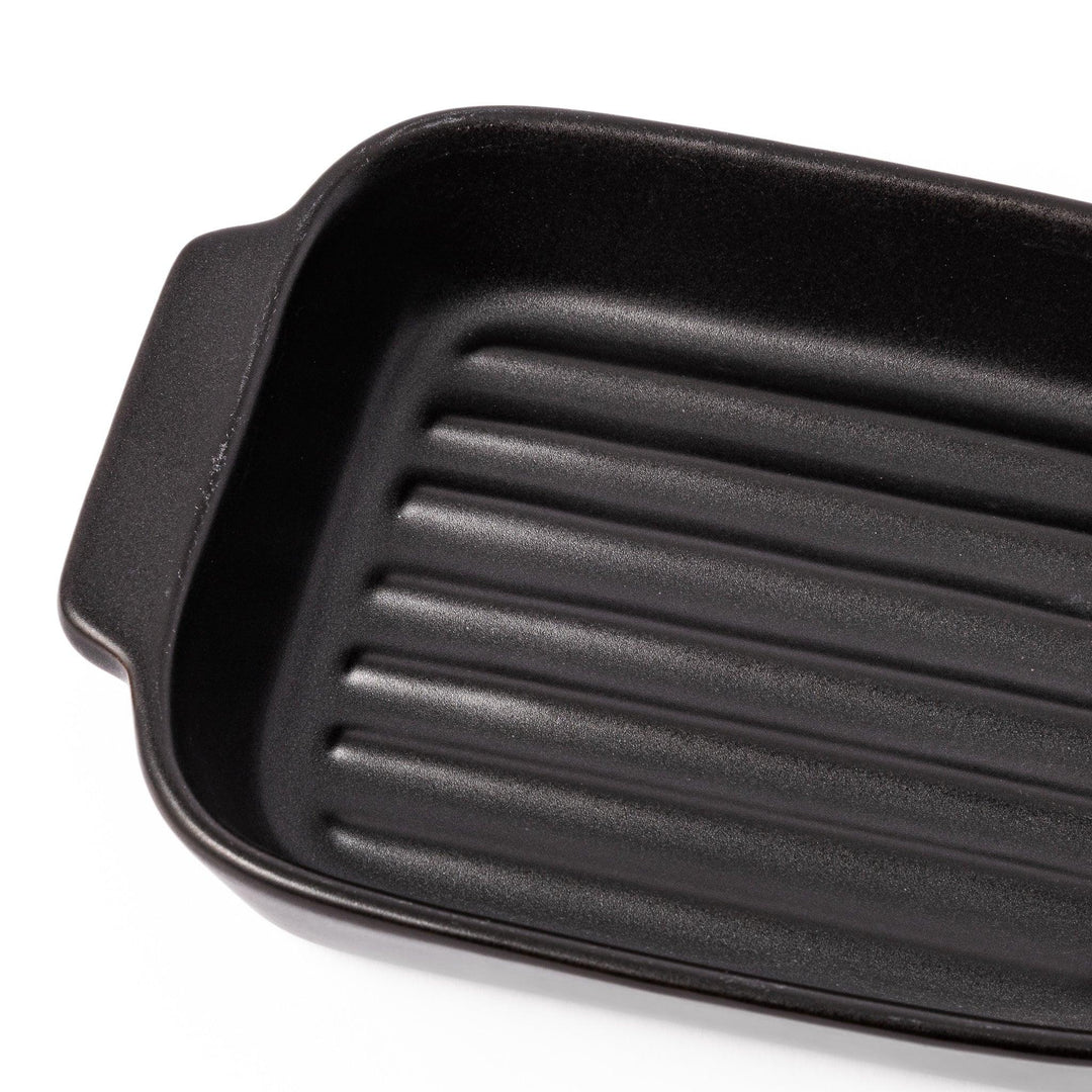 Rectangular black ceramic baking dish with ridged base and side handle, designed for oven use and versatile table presentation.