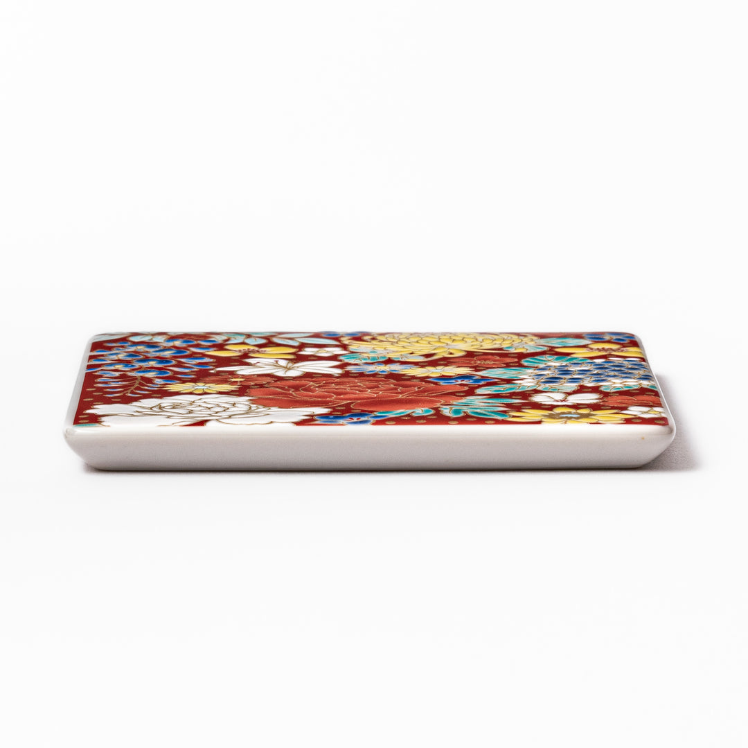 Square Japanese ceramic coaster with vivid red base featuring peony, chrysanthemum, and floral motifs in multicolor design.