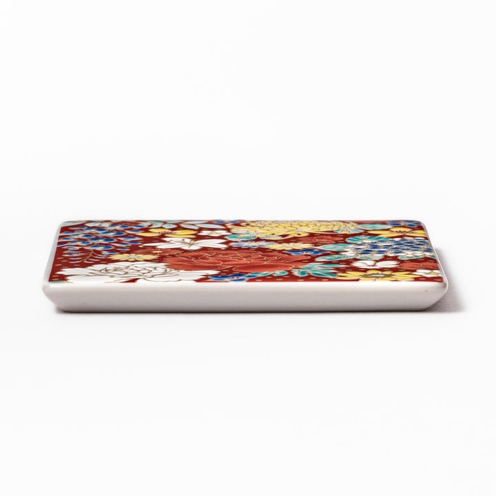 Square Japanese ceramic coaster with vivid red base featuring peony, chrysanthemum, and floral motifs in multicolor design.