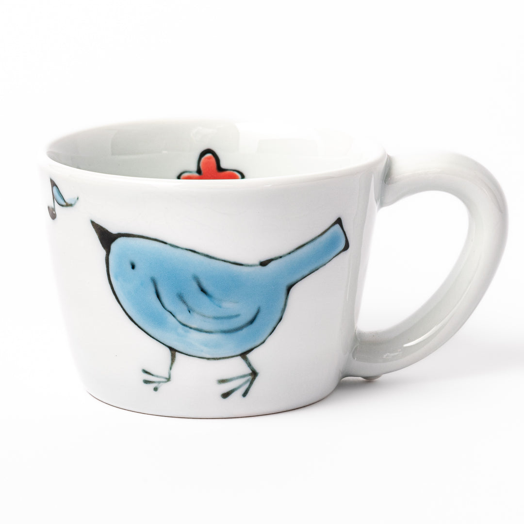 Japanese children’s mug featuring a hand-painted blue bird and musical note design on white porcelain, crafted for little hands to enjoy warm drinks with joy.