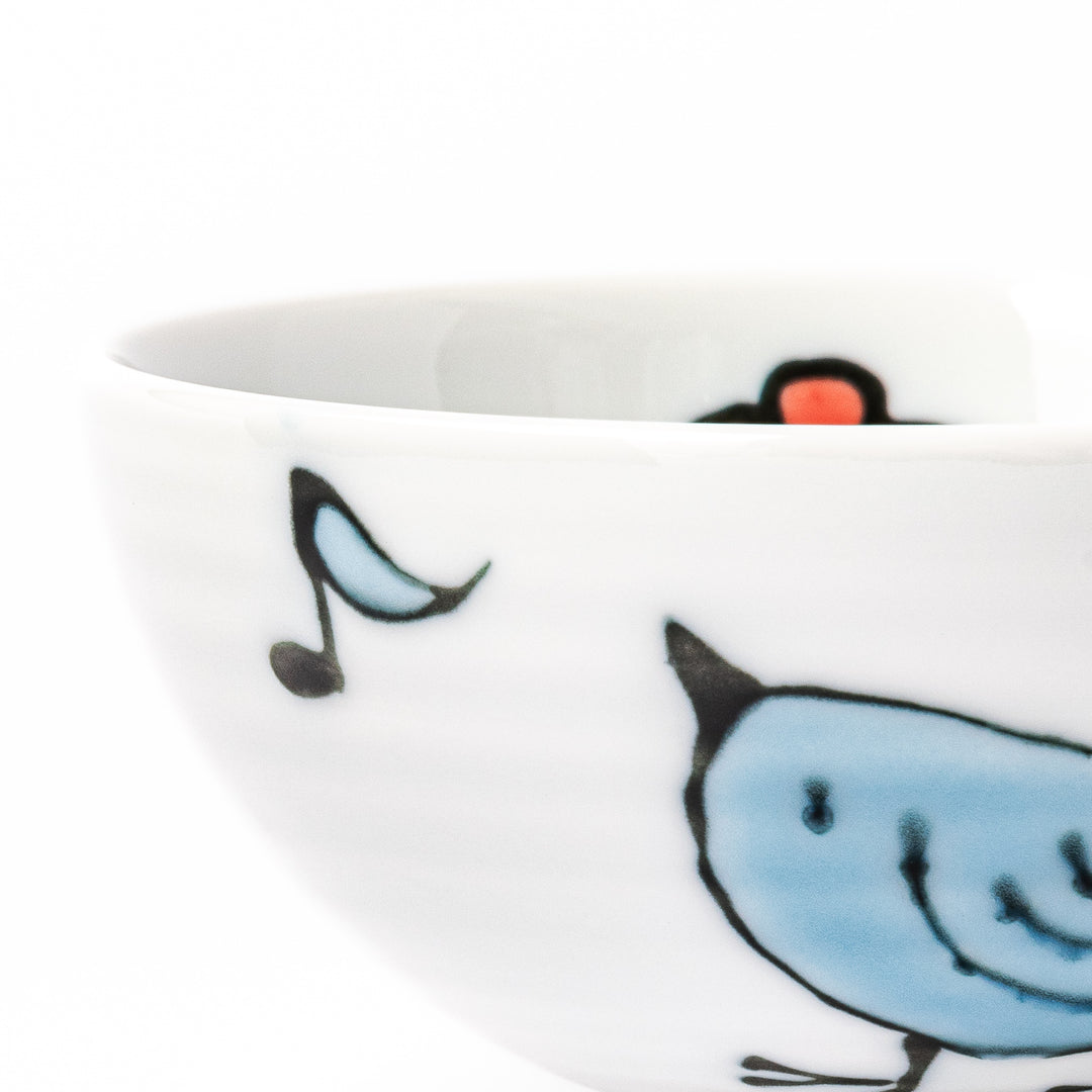 Japanese children’s rice bowl featuring a hand-painted blue bird and musical note motif on white porcelain, designed to bring a cheerful touch to everyday meals.