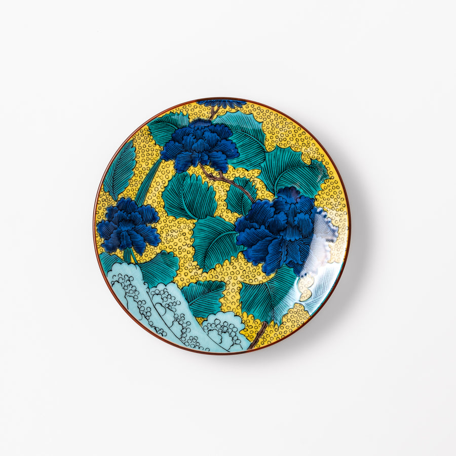 Porcelain dessert plate with bold blue peony flowers, green leaves, and a golden yellow background accented by intricate dot patterns.