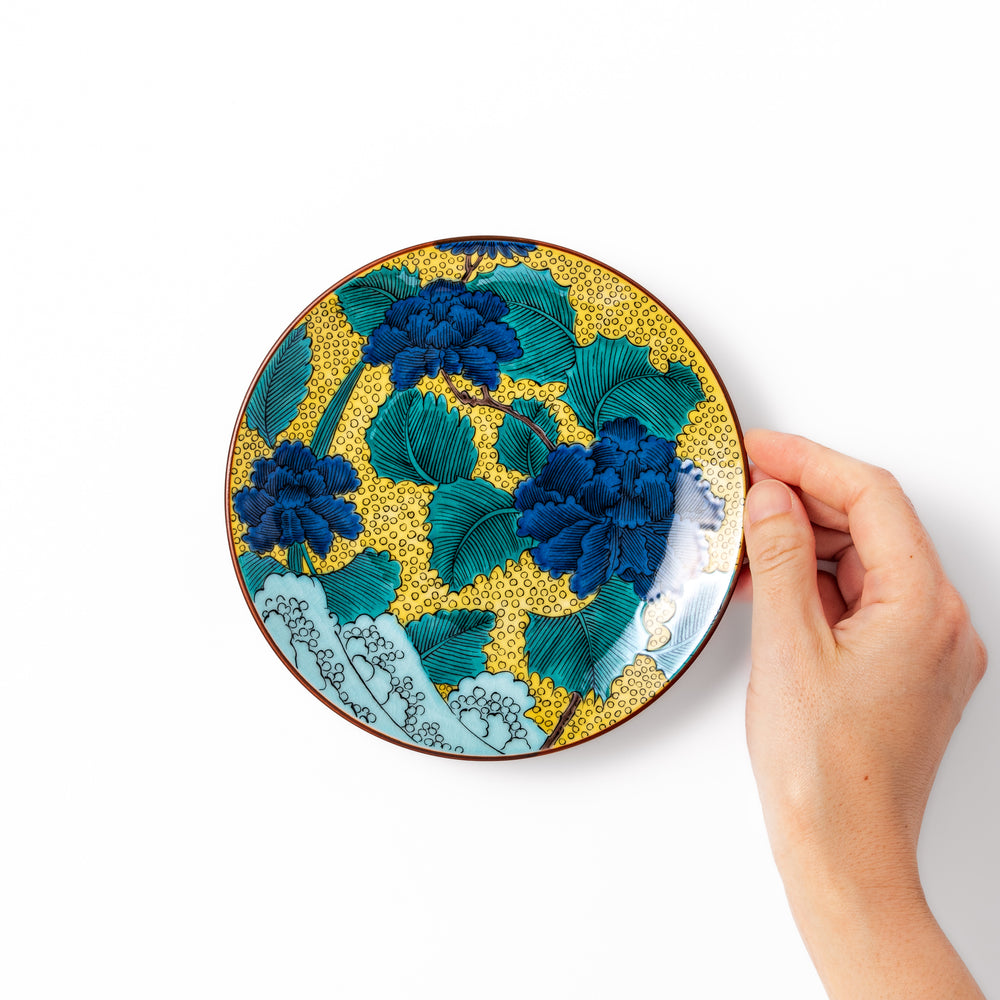 Porcelain dessert plate with bold blue peony flowers, green leaves, and a golden yellow background accented by intricate dot patterns.