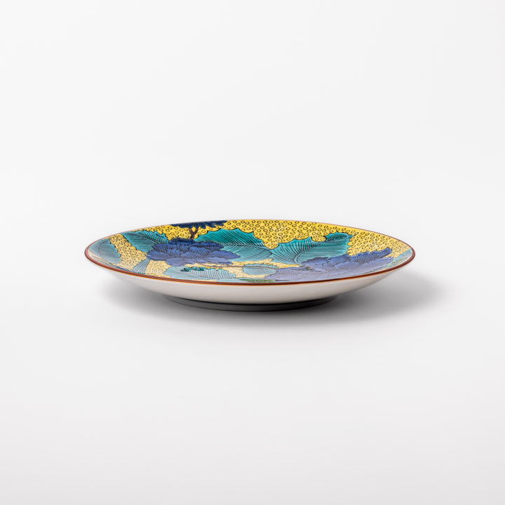 Porcelain dessert plate with bold blue peony flowers, green leaves, and a golden yellow background accented by intricate dot patterns.