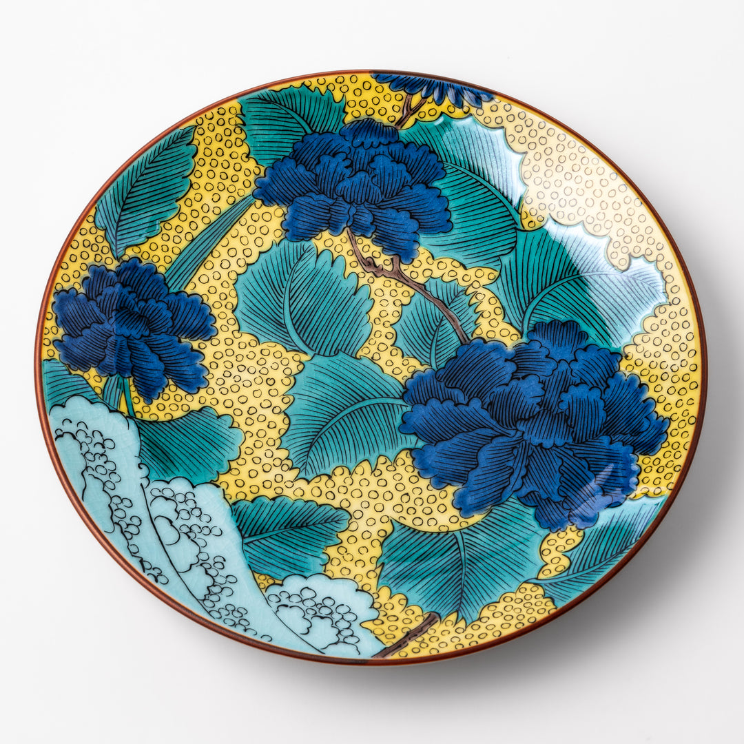 Porcelain dessert plate with bold blue peony flowers, green leaves, and a golden yellow background accented by intricate dot patterns.