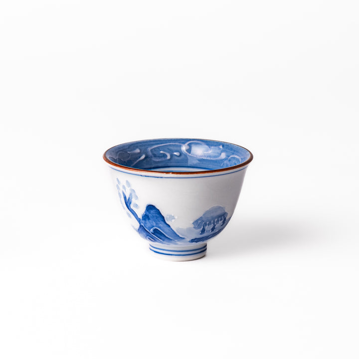 Porcelain sake cup with hand-painted blue mountain and cloud motifs, featuring a red rim and classic Japanese design.