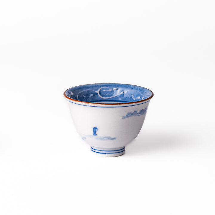 Porcelain sake cup with hand-painted blue mountain and cloud motifs, featuring a red rim and classic Japanese design.