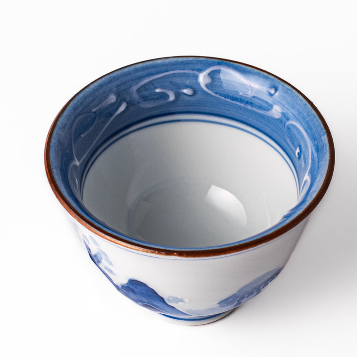 Porcelain sake cup with hand-painted blue mountain and cloud motifs, featuring a red rim and classic Japanese design.