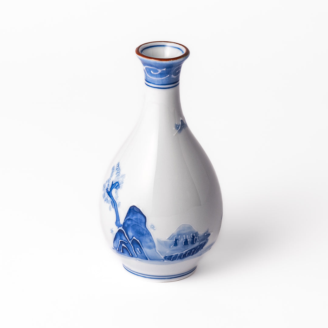 Porcelain sake flask with hand-painted blue mountain and village scenery, featuring a red rim and elegant traditional silhouette.