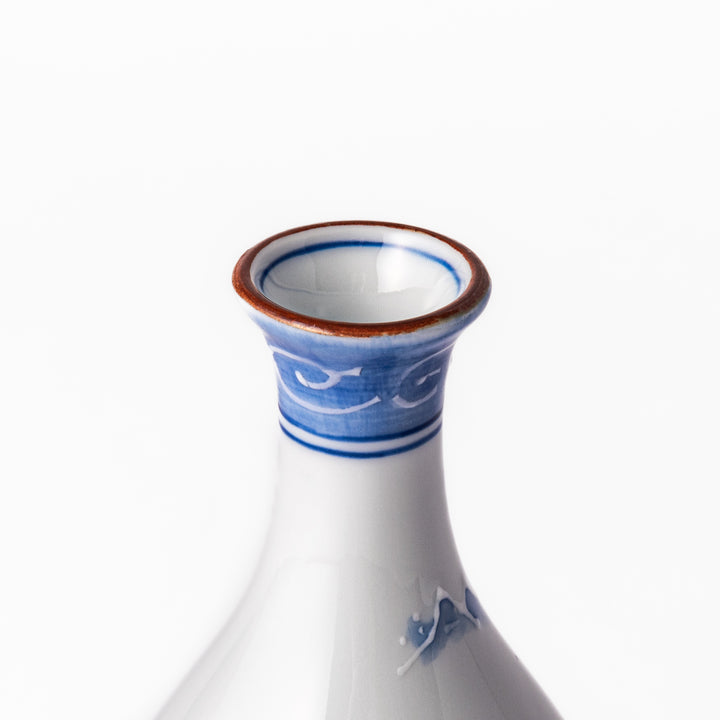 Porcelain sake flask with hand-painted blue mountain and village scenery, featuring a red rim and elegant traditional silhouette.