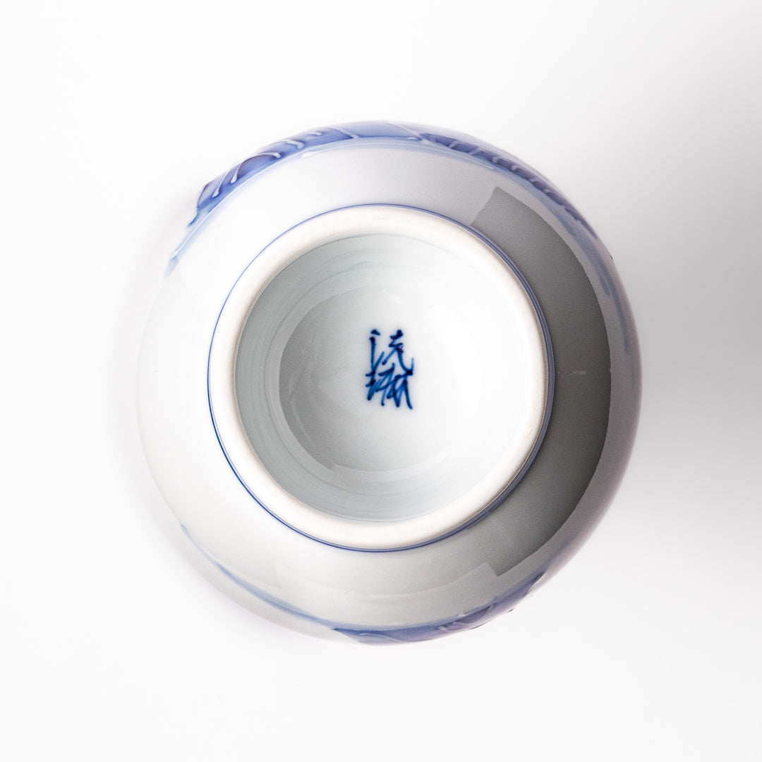 Porcelain sake flask with hand-painted blue mountain and village scenery, featuring a red rim and elegant traditional silhouette.