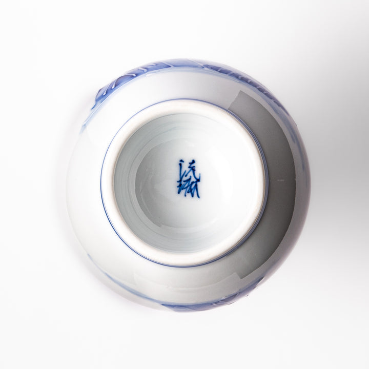 Porcelain sake flask with hand-painted blue mountain and village scenery, featuring a red rim and elegant traditional silhouette.