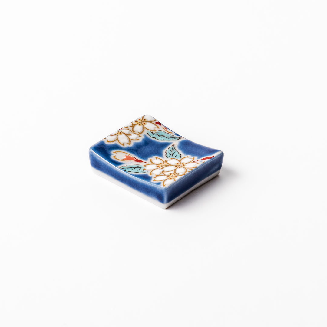Rectangular blue Japanese ceramic chopstick rest with delicate white sakura blossoms and green leaves, ideal for traditional dining.