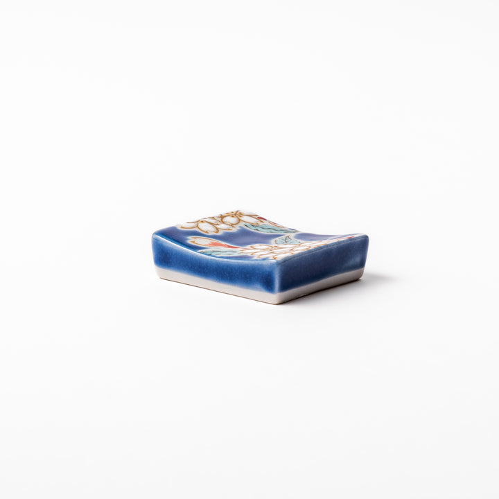 Rectangular blue Japanese ceramic chopstick rest with delicate white sakura blossoms and green leaves, ideal for traditional dining.