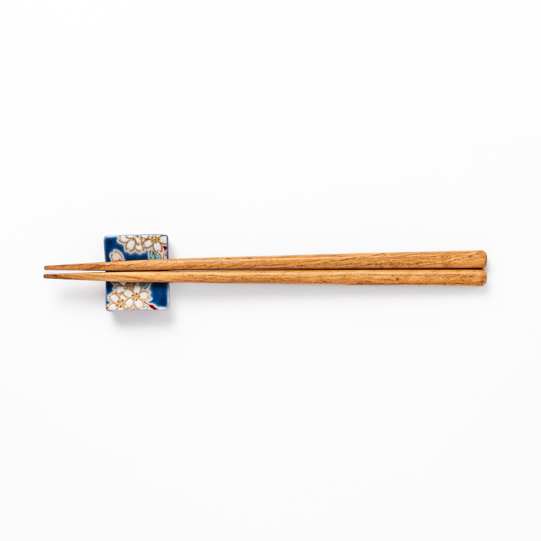 Rectangular blue Japanese ceramic chopstick rest with delicate white sakura blossoms and green leaves, ideal for traditional dining.