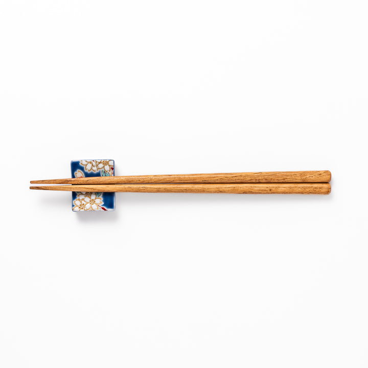 Rectangular blue Japanese ceramic chopstick rest with delicate white sakura blossoms and green leaves, ideal for traditional dining.