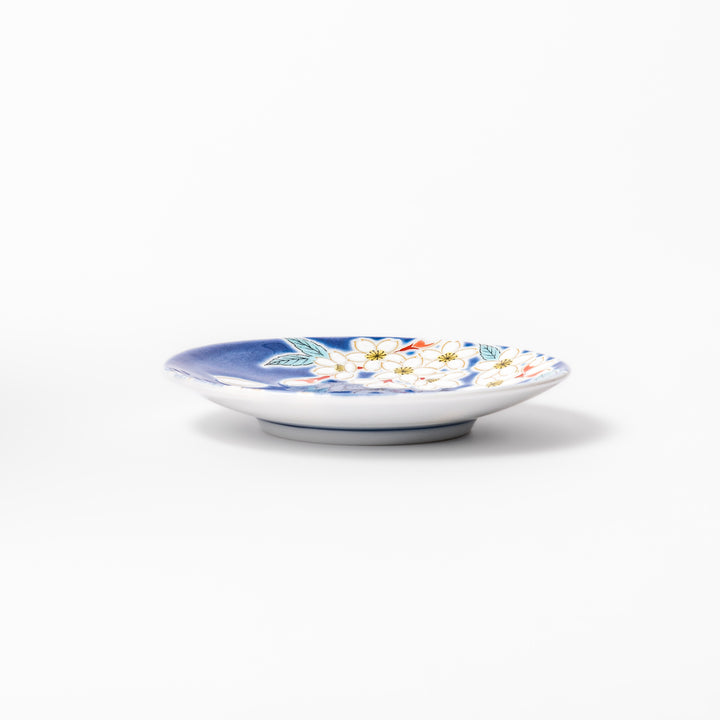 Blue Japanese ceramic sauce dish adorned with white sakura blossom and petals, ideal for traditional dining and serving soy sauce or condiments.