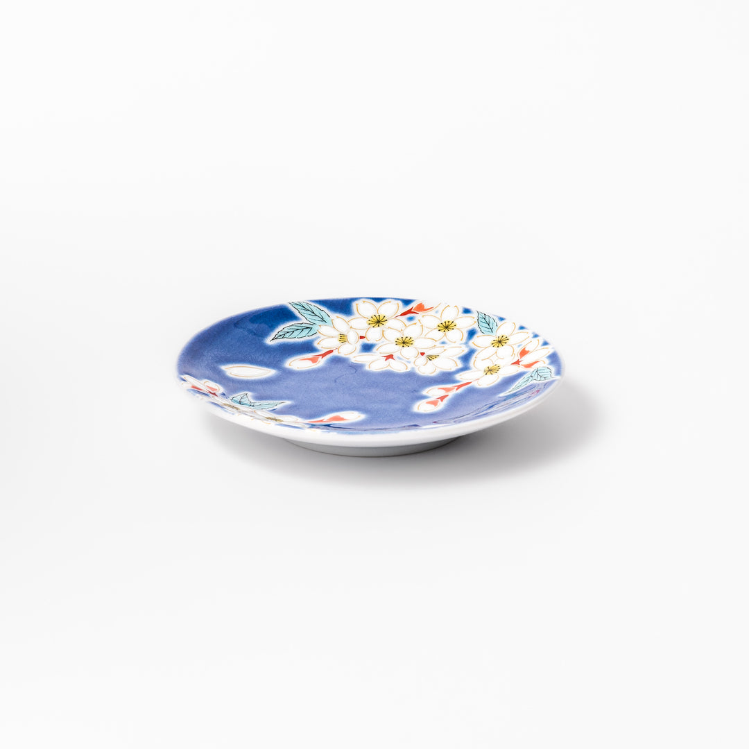 Blue Japanese ceramic sauce dish adorned with white sakura blossom and petals, ideal for traditional dining and serving soy sauce or condiments.