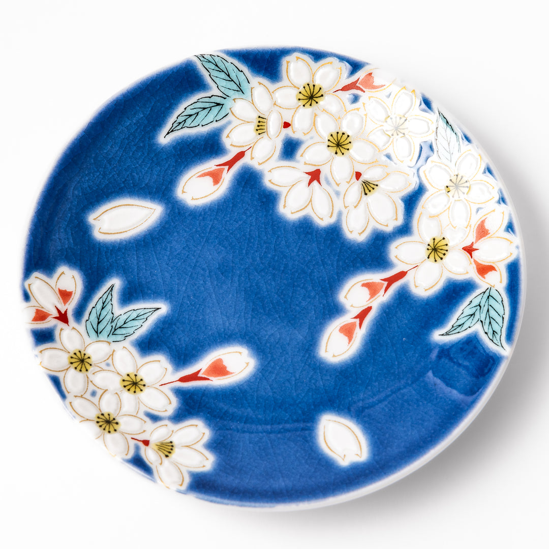 Blue Japanese ceramic sauce dish adorned with white sakura blossom and petals, ideal for traditional dining and serving soy sauce or condiments.