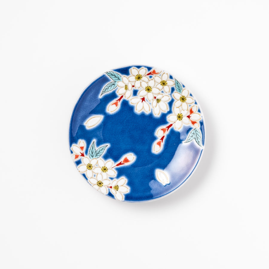 Blue Japanese ceramic sauce dish adorned with white sakura blossom and petals, ideal for traditional dining and serving soy sauce or condiments.