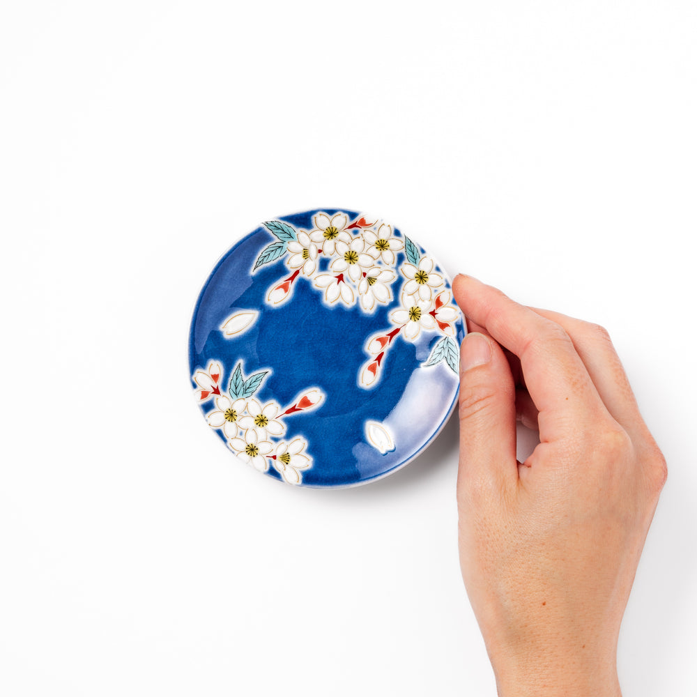 Blue Japanese ceramic sauce dish adorned with white sakura blossom and petals, ideal for traditional dining and serving soy sauce or condiments.