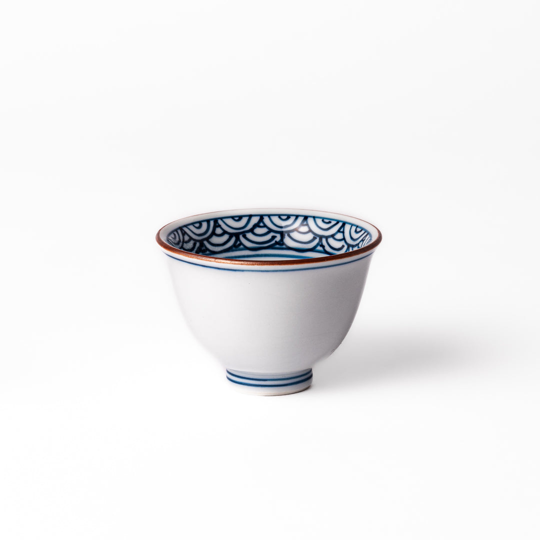 Porcelain sake cup with a white exterior and interior featuring traditional blue wave patterns and a warm brownish rim.