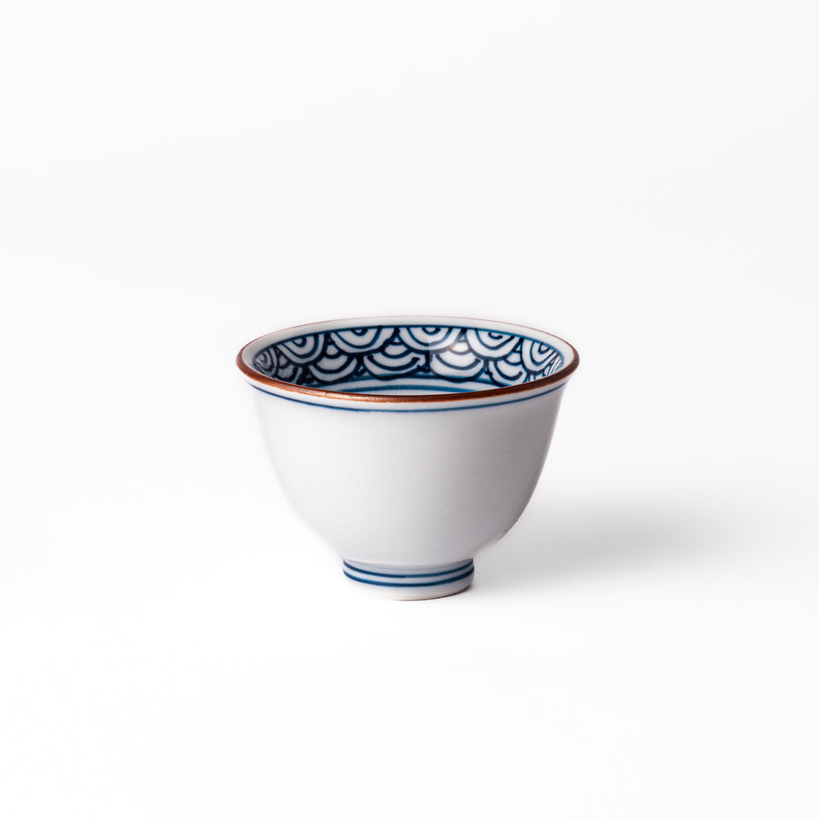 Porcelain sake cup with a white exterior and interior featuring traditional blue wave patterns and a warm brownish rim.