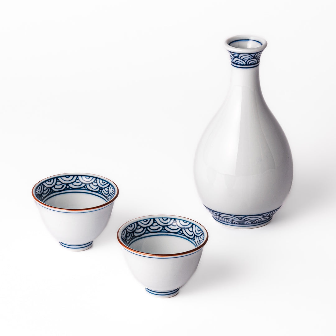 Three piece porcelain sake set with a white flask and two cups featuring traditional blue wave patterns and reddish brown rims.