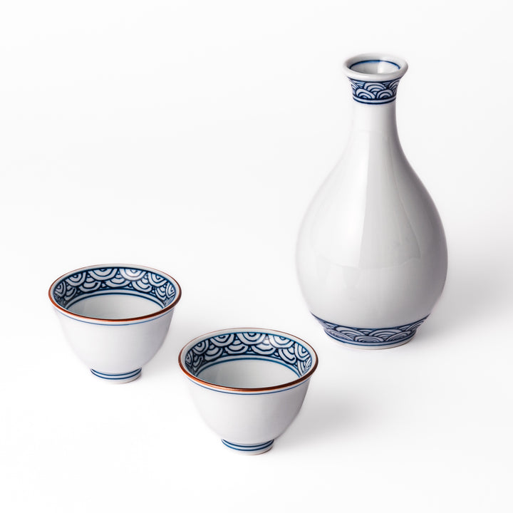 Three piece porcelain sake set with a white flask and two cups featuring traditional blue wave patterns and reddish brown rims.