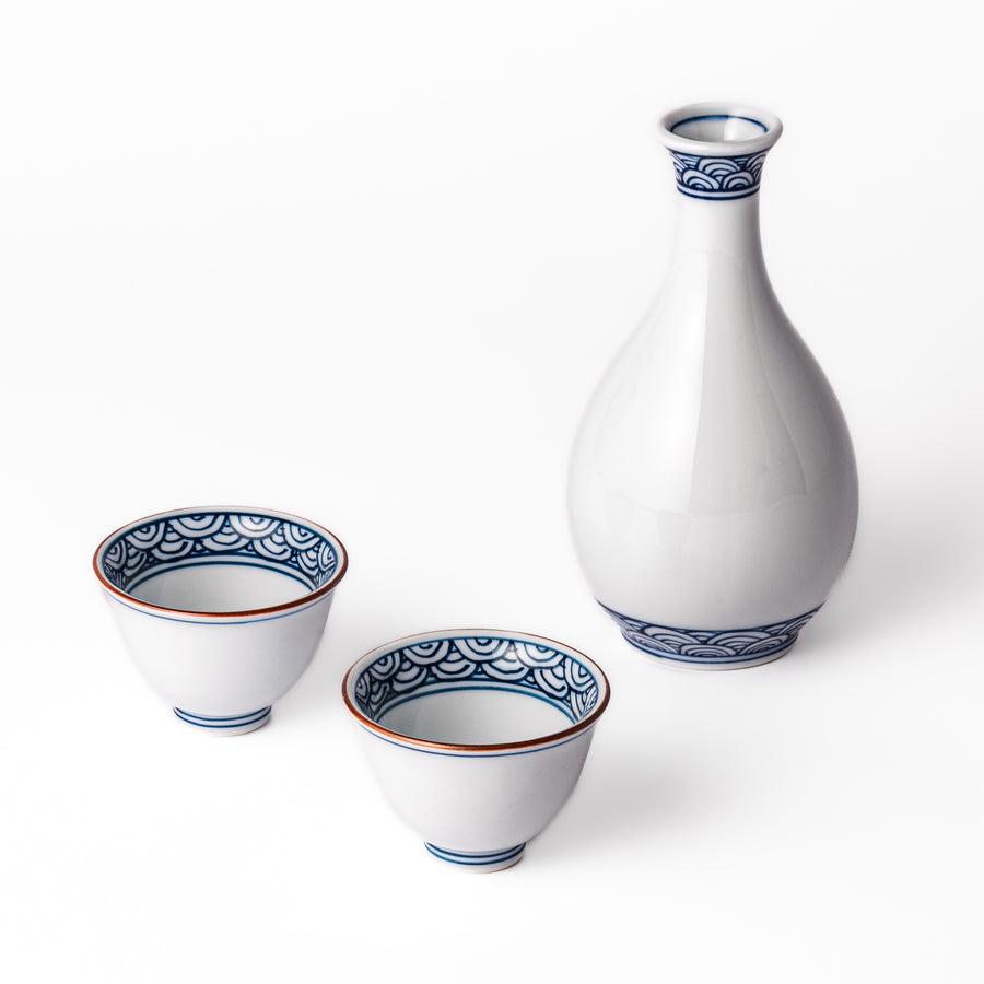 Three piece porcelain sake set with a white flask and two cups featuring traditional blue wave patterns and reddish brown rims.